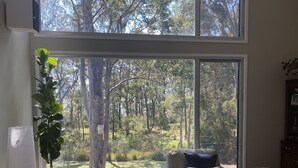 Ein Wohnzimmer mit großem Fenster und Blick auf einen Wald, inklusive Sofa, Sessel und einem kleinen Tisch.