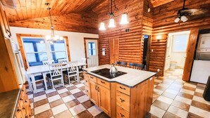 Interno di una baita con cucina, caratterizzato da un pavimento a scacchi, mobili in legno e un'isola centrale con un piano cottura.
