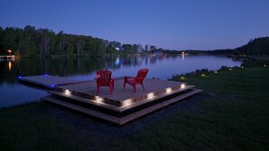 Un molo di legno con due sedie rosse e un tavolo, immerso in un'acqua calma e circondato da alberi.