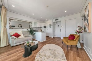 Ein modernes Wohnzimmer mit einer Couch, einem Couchtisch, einem Teppich, einem Sessel und einer Küchenzeile mit Schränken und einer Uhr.