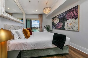 Ein Schlafzimmer mit einem Bett, einem großen Spiegel, einer Chandelierleuchtre und einem Blumenbild.