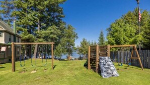 A backyard with a swing set, a slide, and a wooden fence. - Enjoy a Relaxing Couples Getaway and Lakeside View at Stievater's Lakeside Cottages! (Inlet)