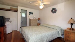 A bedroom with a bed, a ceiling fan, a dresser, a microwave, and a door leading to another room. - Enjoy a Relaxing Couples Getaway and Lakeside View at Stievater's Lakeside Cottages! (Inlet)