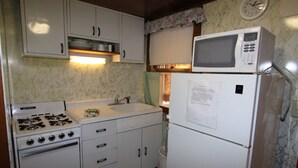 A compact kitchen with white cabinets, a stove, a sink, a microwave, and a refrigerator. - Lakeside Getaway, Just Steps Away from Fourth Lake Here at Stiefvater's Lakeside Cottages! (Inlet)