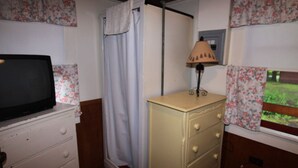 A room with a television on a dresser, a lamp, a shower curtain, and floral curtains. - Lakeside Getaway, Just Steps Away from Fourth Lake Here at Stiefvater's Lakeside Cottages! (Inlet)