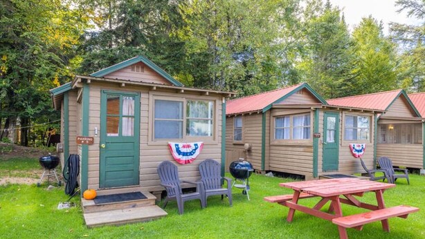 A small cabin with a green door, a barbecue grill, and a picnic table. - Lakeside Getaway, Just Steps Away from Fourth Lake Here at Stiefvater's Lakeside Cottages! (Inlet)