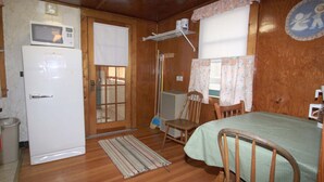 Een compacte kamer met een bed, een tafeltje, een stoel, een magnetron en een koelkast.