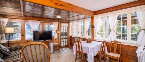 A cozy cabin interior with a wooden ceiling, a television, a dining table with chairs, and a sofa.