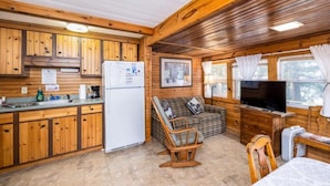 Ein Blockhaus-Interieur mit Holzwänden, einer Küchenzeile, einem Sofa, einem Fernseher und einem Essbereich.