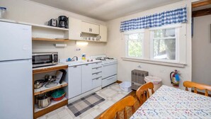 Cocina compacta con refrigerador, microondas, estufa y lavamanos. Hay una ventana con cortina a cuadros, y un extintor de incendios montado en la pared.