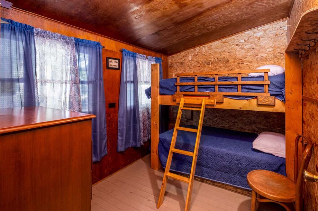Une chambre avec un lit superposé, une petite échelle en bois, une petite chaise en bois et un bureau.
