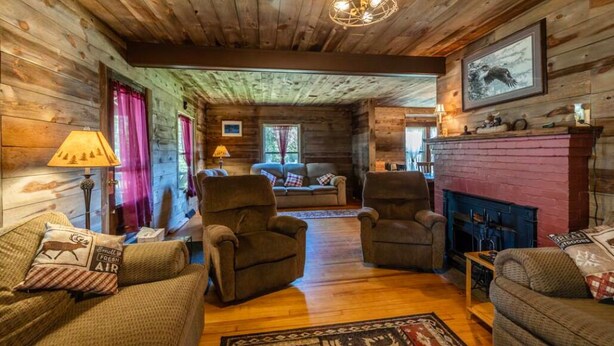 A cozy cabin interior with wooden walls, a fireplace, and a comfortable seating area with two armchairs and a sofa. - Lakeside House View Overlooking Beautiful 4th Lake Here at Stiefvater's Lakeside Cottages (Inlet)