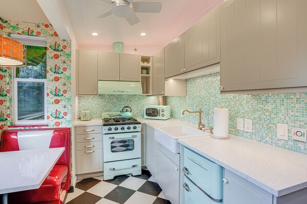 Une cuisine au style rétro, avec un carrelage à motifs, des appareils électroménagers anciens et des meubles de couleur pastel.