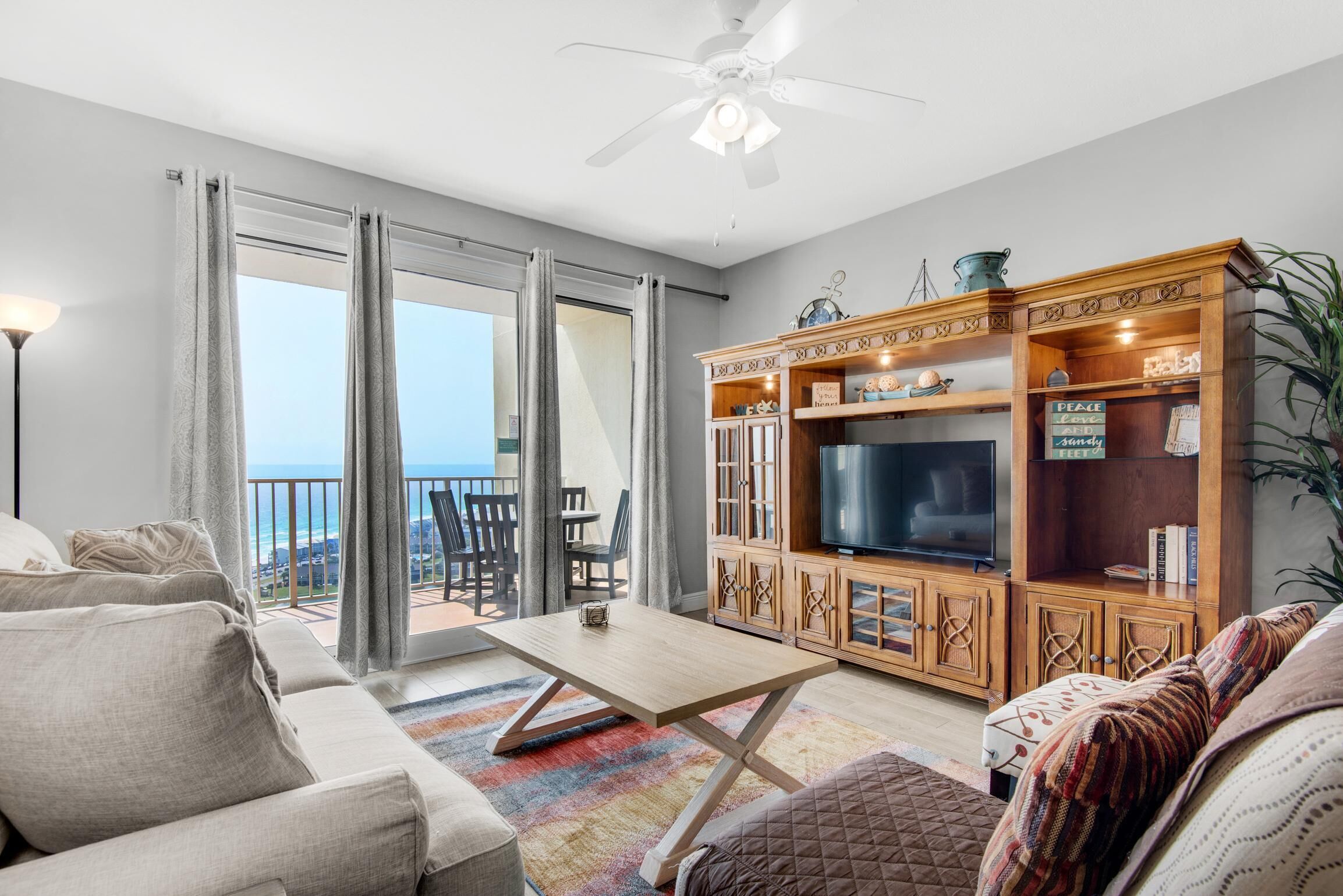 A living room with a sofa, coffee table, TV, wooden cabinet, and a balcony with a view.