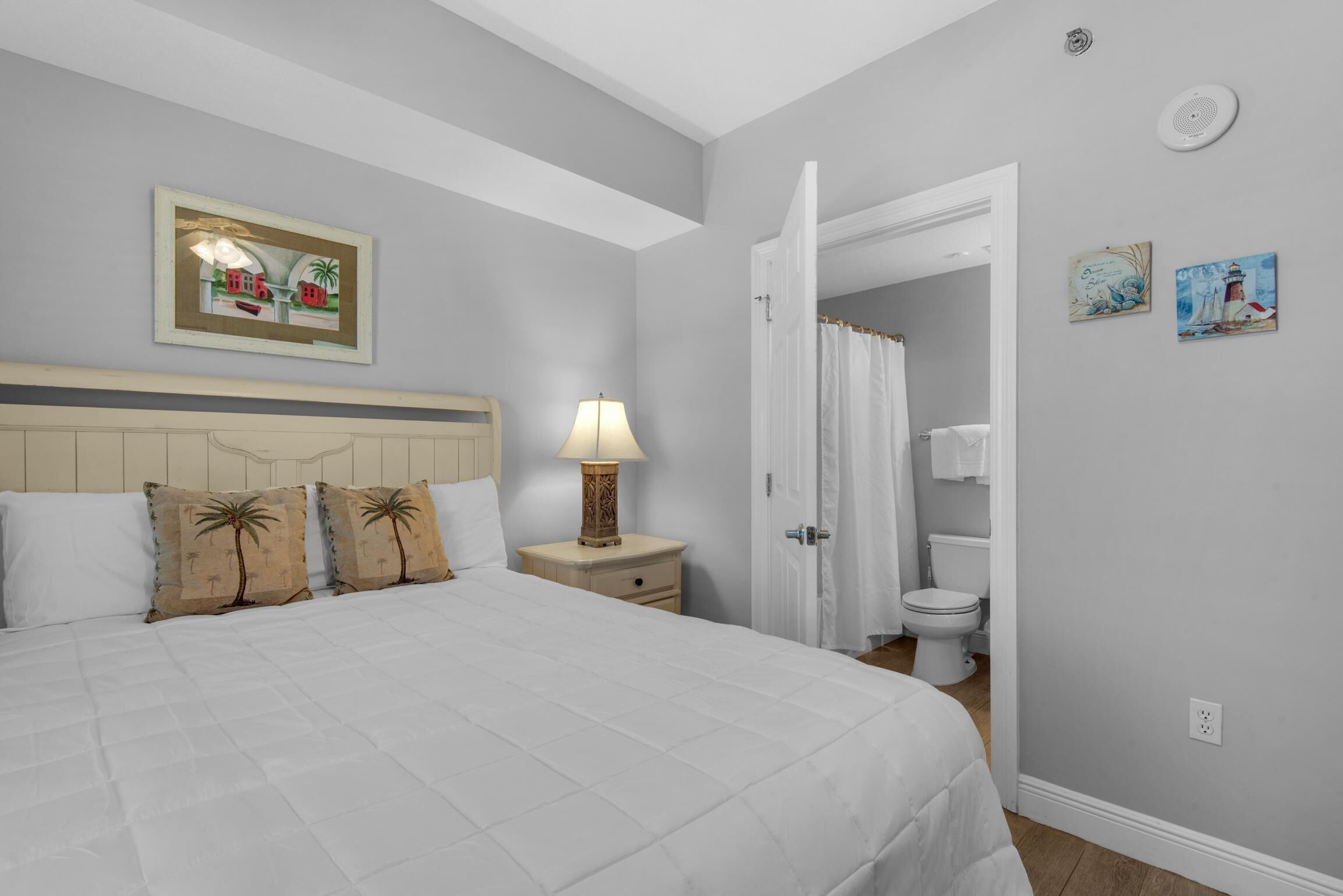 A bedroom with a bed, nightstand, lamp, and a door leading to a bathroom.