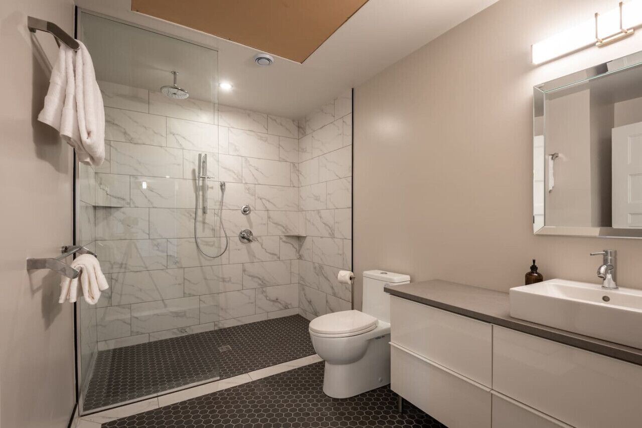 Ein modernes Badezimmer mit einer Duschkabine, einer Toilette und einem Waschbecken mit Spiegel.