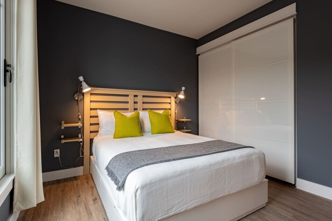 Une chambre à coucher moderne avec un grand lit, une tête de lit dotée d’un éclairage intégré, une table de chevet et une porte de placard coulissante.