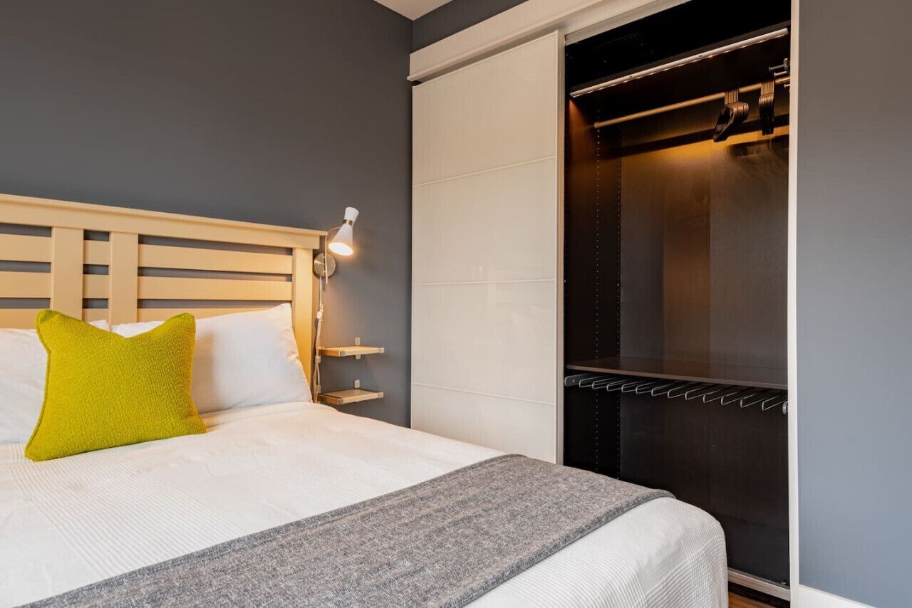 A hotel room with a bed, a nightstand, a lamp, a wardrobe, and a sliding door closet.