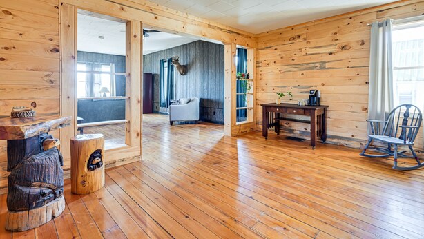 Une pièce spacieuse aux murs et au plancher en bois, avec un fauteuil à bascule, un bureau et une chaise.