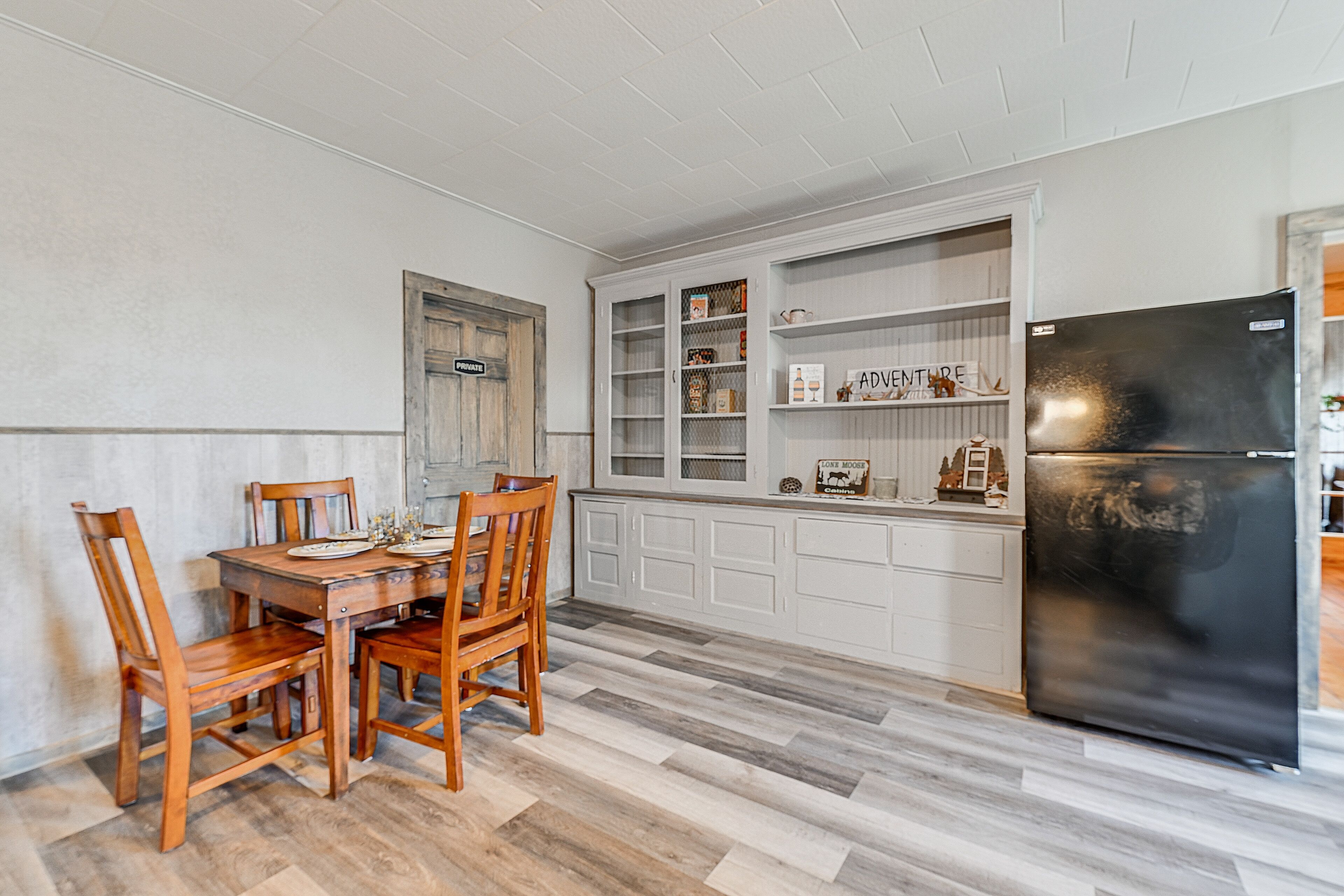A kitchen with a wooden dining table and chairs, white cabinetry, and a black refrigerator.