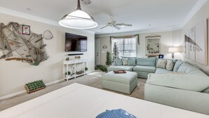 A living room with a sectional sofa, a flat-screen TV, a ceiling fan, and a wall-mounted fish net decoration. - Townhome w/ Outdoor Pool & White Lake Access! (Elizabethtown)