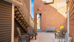 A narrow outdoor corridor with wooden steps, a brick wall, and outdoor seating including Adirondack chairs and a bench. - Suite 203- Spacious two Bedroom apartment-style Suite in Hybrid Hotel Wolfville (Wolfville)