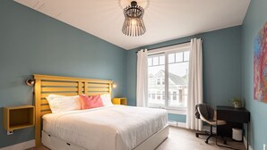 A bedroom with a bed, a desk, a chair, a window, and a ceiling light. - Suite 203- Spacious two Bedroom apartment-style Suite in Hybrid Hotel Wolfville (Wolfville)