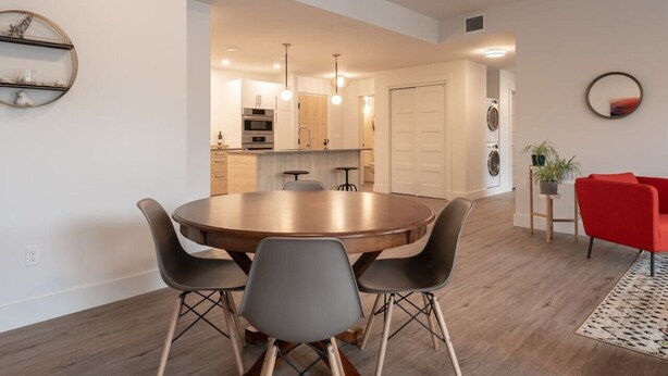 A modern kitchen with a central island, a dining area with a round table and chairs, and a red accent chair. - Suite 203- Spacious two Bedroom apartment-style Suite in Hybrid Hotel Wolfville (Wolfville)