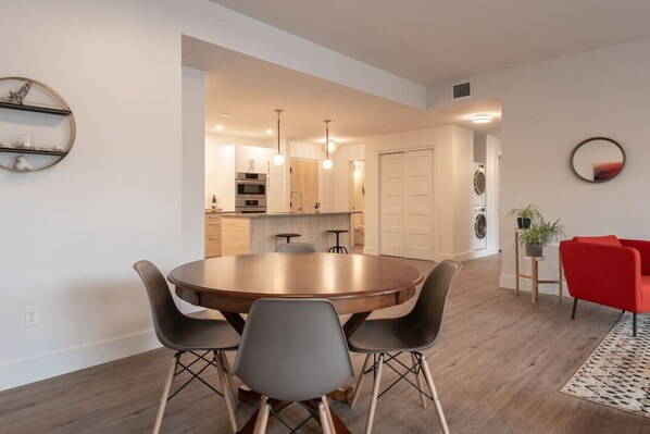 Een moderne keuken met een centraal eiland, een eethoek met een ronde tafel en stoelen, en een rode accentstoel.