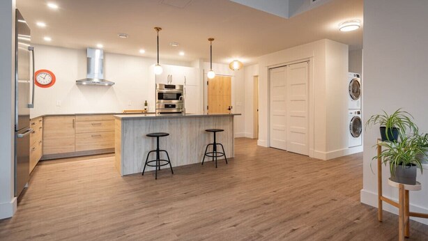 A modern kitchen with wooden cabinets, a central island with stools, stainless steel appliances, and pendant lighting. - Suite 203- Spacious two Bedroom apartment-style Suite in Hybrid Hotel Wolfville (Wolfville)