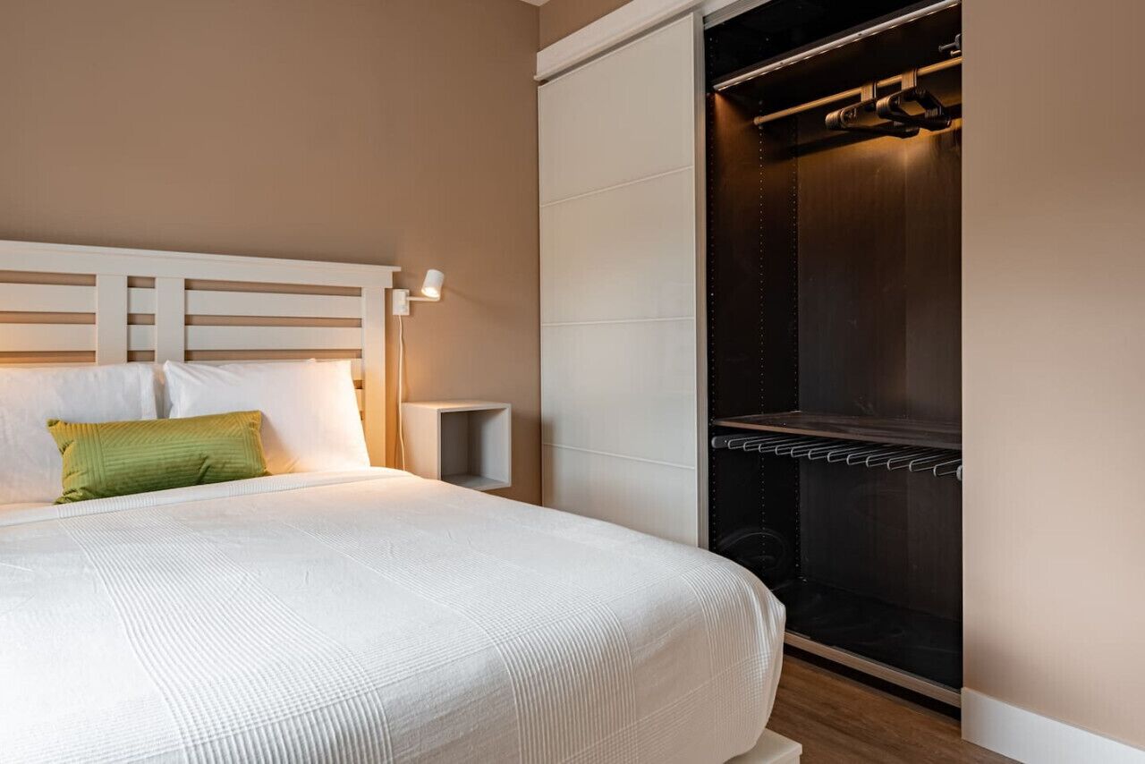 A neatly made bed with a white headboard, a green pillow, and a bedside table with a lamp.