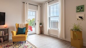 A bright living room with a yellow armchair, a large window, and a view of the outdoors. - Suite 302 - 470 Main (Wolfville)