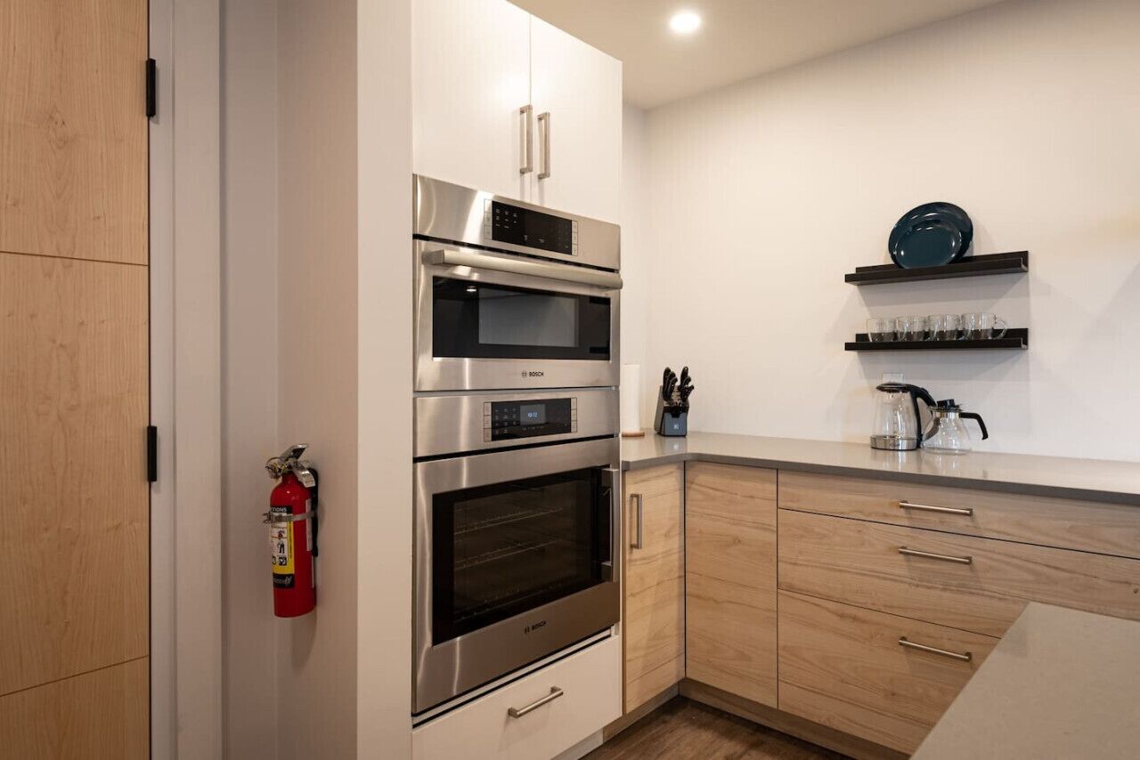 Una cocina moderna con electrodomésticos de acero inoxidable, armarios de madera y una estantería empotrada con vasos y una tetera.