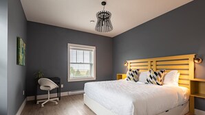 A bedroom with a bed, a desk, a chair, a window, and a pendant light. - Suite 302 - 470 Main (Wolfville)