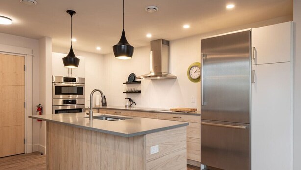 A modern kitchen with a central island, stainless steel appliances, and pendant lighting. - Suite 302 - 470 Main (Wolfville)