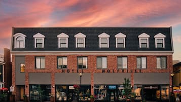 A two-story building with a brick facade, multiple storefronts on the ground floor, and a clear sky with pink and purple hues.