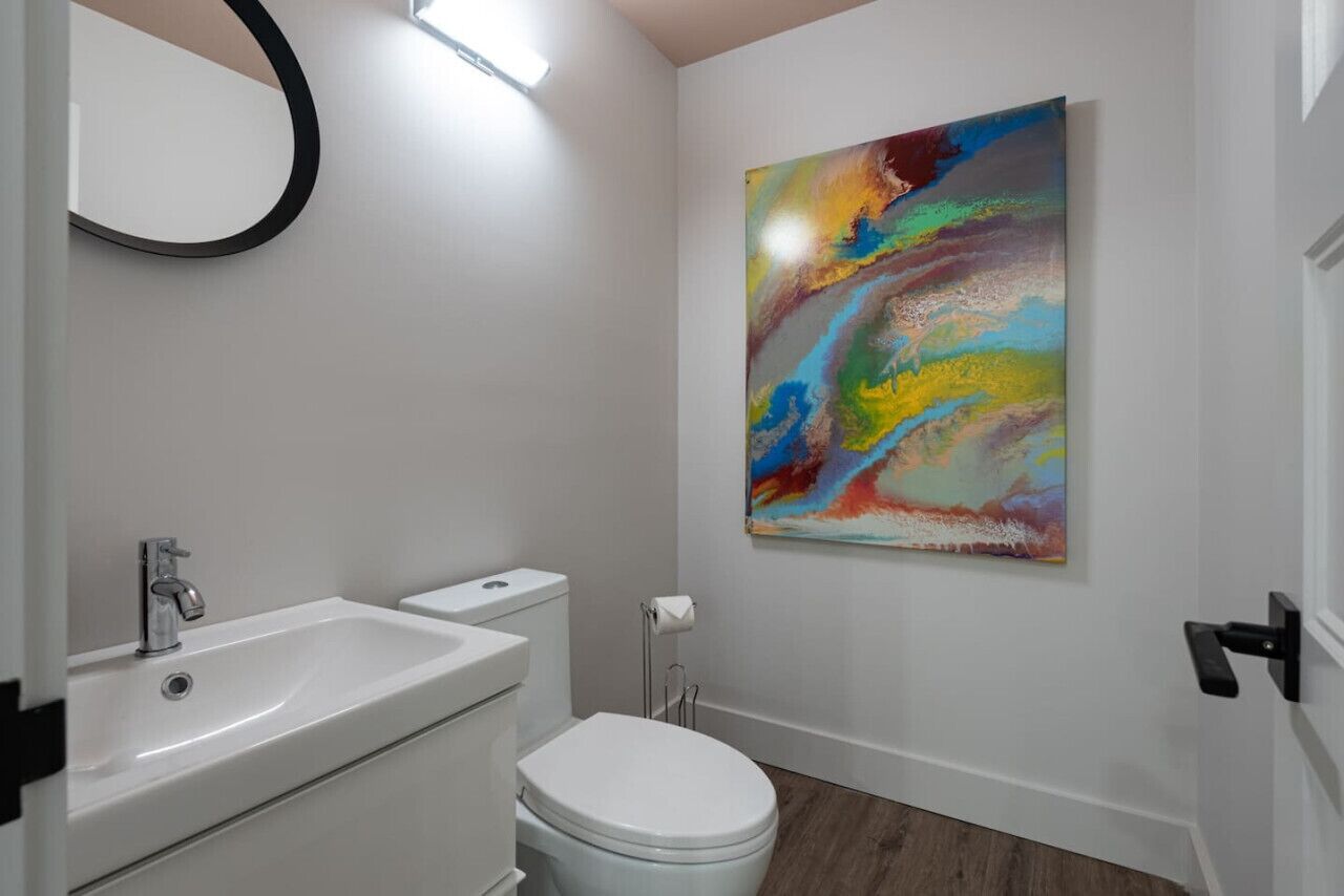 A modern bathroom with a white sink, toilet, and a colorful abstract painting on the wall.