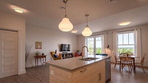 A modern kitchen with a central island, pendant lighting, and a dining area with wooden chairs. - Suite 304 - 470 Main (Wolfville)