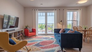 A modern living room with a television, a sofa, a red chair, and a balcony with a view. - Suite 304 - 470 Main (Wolfville)