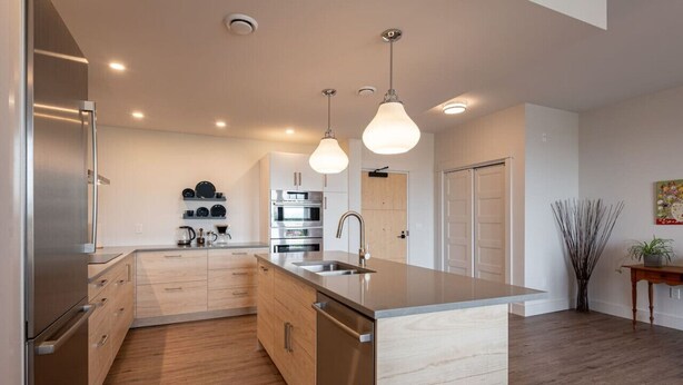 A modern kitchen with stainless steel appliances, wooden cabinets, and pendant lighting. - Suite 304 - 470 Main (Wolfville)