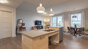 A modern kitchen with a central island, pendant lighting, and a dining area with a table and chairs. - Suite 204- Two Bedroom apartment-style Suite w Balcony in Hybrid Hotel Wolfville (Wolfville)