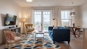 A modern living room with a sofa, a chair, a TV, and a dining area with a table and chairs. - Suite 204- Two Bedroom apartment-style Suite w Balcony in Hybrid Hotel Wolfville (Wolfville)
