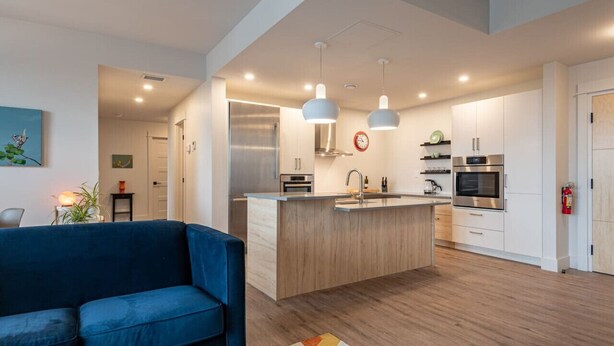 A modern kitchen with a central island, pendant lighting, and stainless steel appliances. - Suite 204- Two Bedroom apartment-style Suite w Balcony in Hybrid Hotel Wolfville (Wolfville)