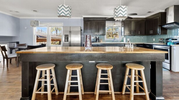 Une cuisine moderne dotée d’un grand îlot central, de meubles de couleur sombre et de tabourets en bois.