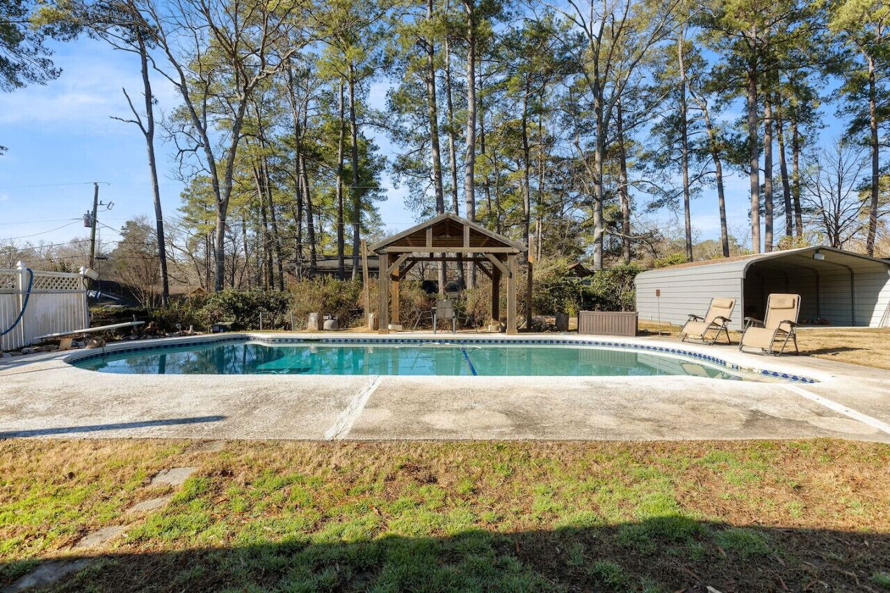 Un jardin avec une piscine, un gazebo en bois et un patio couvert.