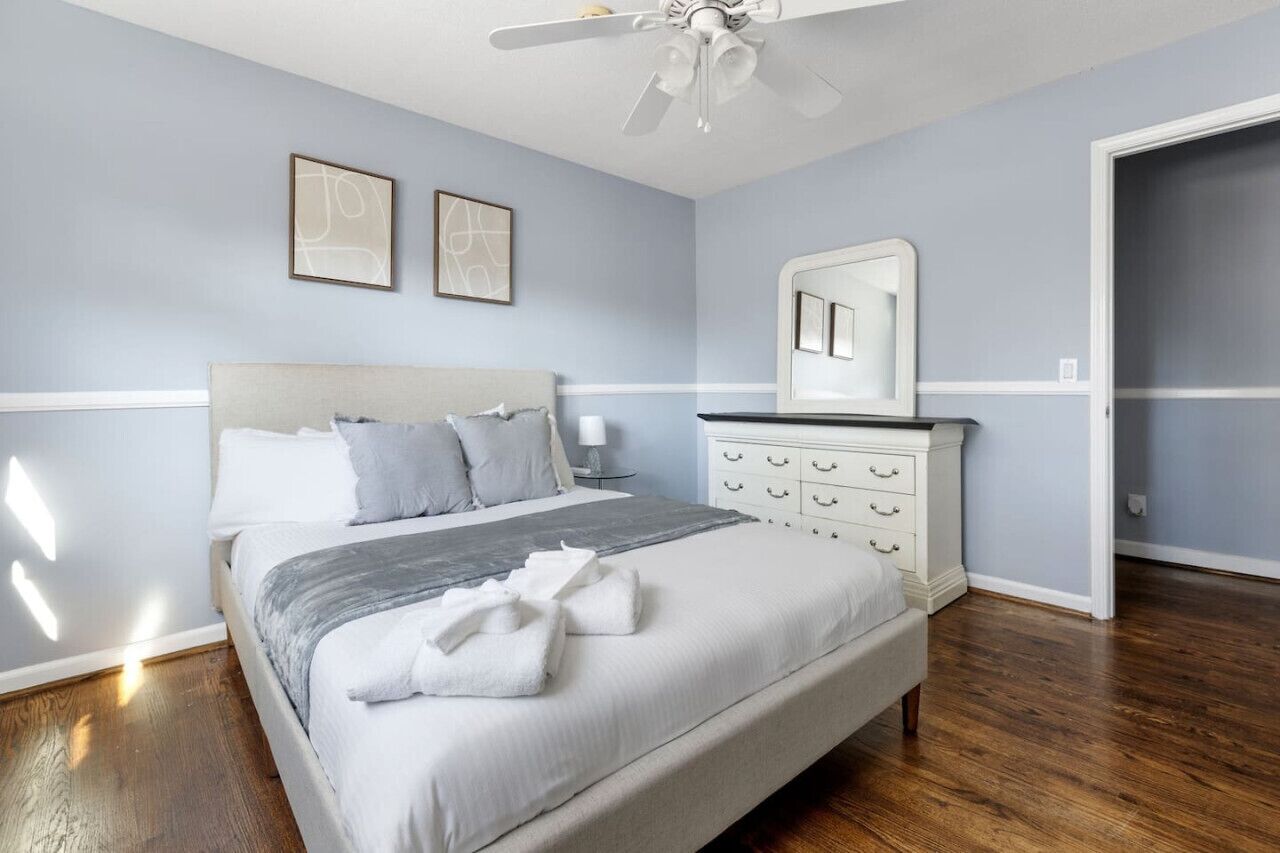 Un dormitorio con cama, cómoda, ventilador de techo y dos cuadros en la pared.