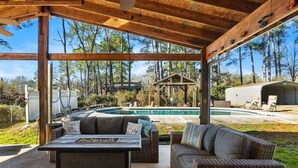 Une terrasse extérieure avec des meubles en osier, une piscine et un kiosque situé dans un espace boisé.