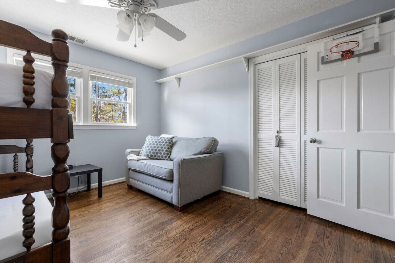 Een kamer met een houten vloer, een grijze bank, een plafondventilator en een witte deur met een basketbalring.
