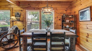 Ein Interieur einer Holzhütte mit einem Holzespeisetisch, Stühlen, einer Chandelüster und Blick durch die Tür.