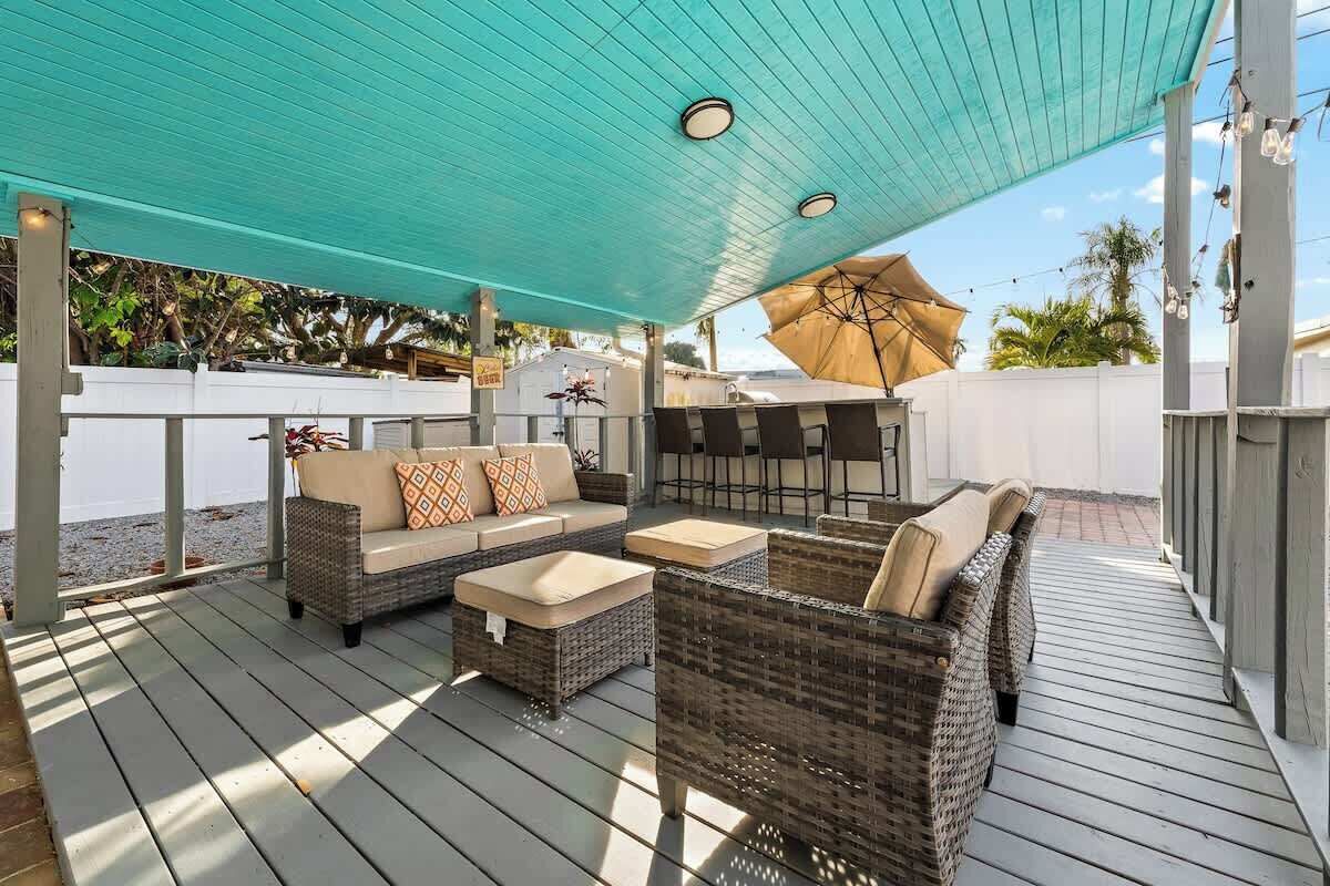 A covered outdoor seating area with wicker furniture and a white fence in the background.